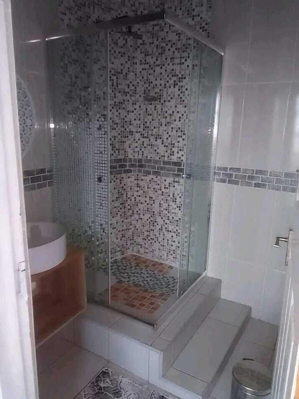 A shower with a glass door, tiled walls, and a small step leading to the shower area. - Ranch Inn Guest House (Hlotse)