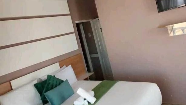 A hotel room with a bed, pillows, a TV, and a door.