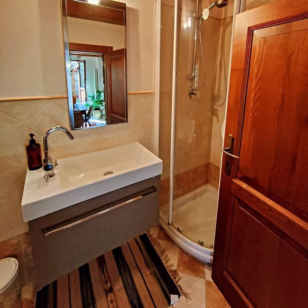 Ein Badezimmer mit weißem Waschbecken, einem Spiegel darüber, einer Duschkabine mit Glastür und einer Holztür.