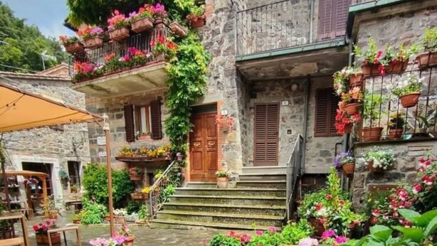 Un bâtiment en pierre avec une porte en bois, des marches menant à un balcon et des plantes en pot.