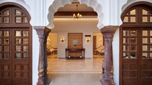 Una entrada imponente con puertas y columnas de madera ornamentadas, que conduce a un interior bien iluminado con un muro decorativo y zona de estar.