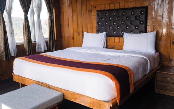 Una habitación con paneles de madera, una cama grande, un banco y una mesita de noche.