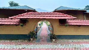 A building with a red-tiled roof and a central archway leading to a paved pathway. - Panchet Residency (Raghunathpur)