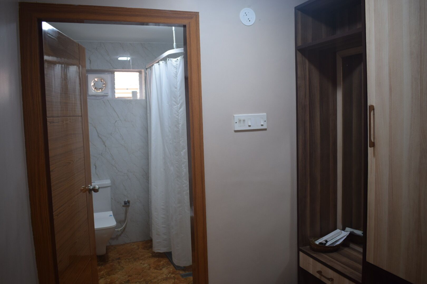 A bathroom with a toilet, shower, and wooden wardrobe.