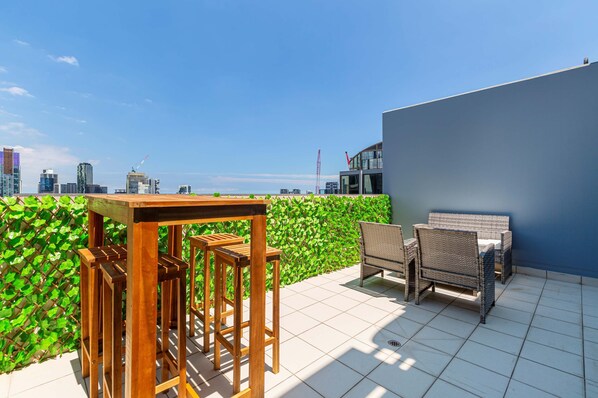 A rooftop terrace with a table and chairs, a blue wall, and a city view.