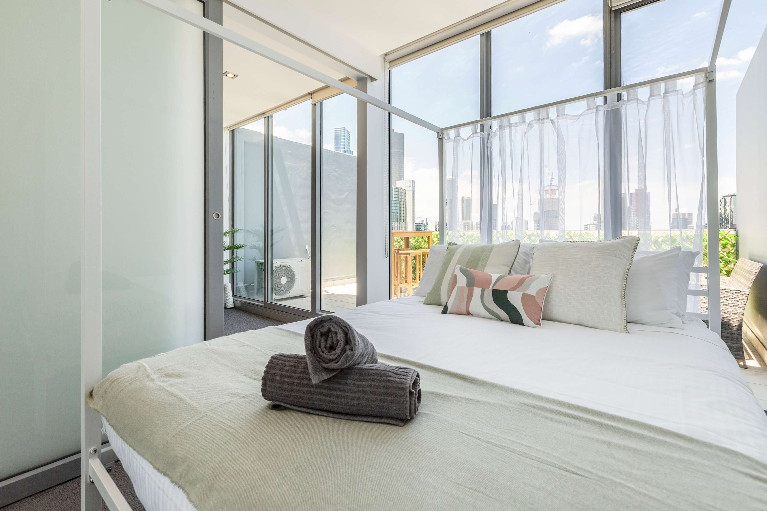 Una habitación de hotel moderna con una cama grande, vistas de la ciudad a través de ventanas de piso a techo y un balcón con vistas.