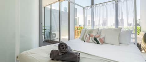 Una habitación de hotel moderna con una cama grande, vistas de la ciudad a través de ventanas de piso a techo y un balcón con vistas.