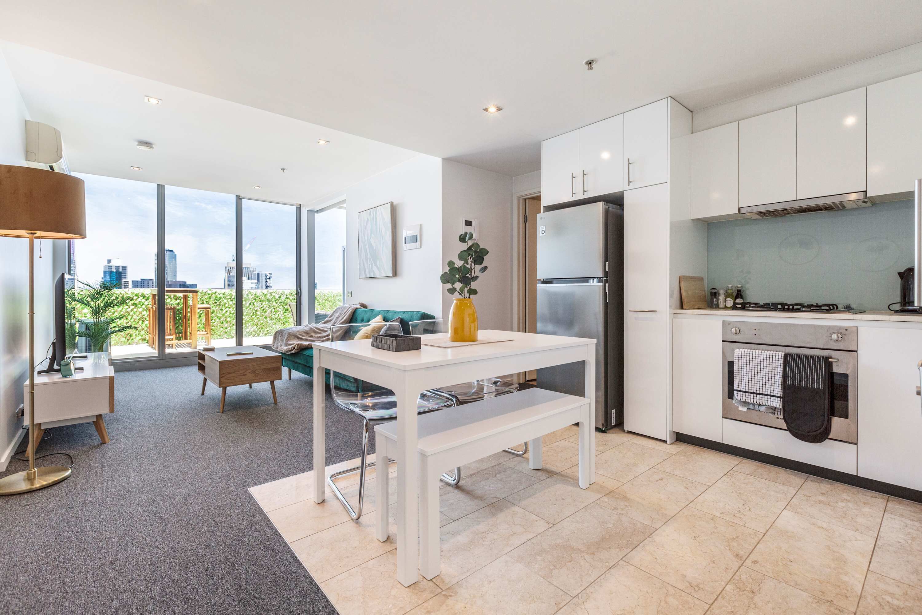 A modern kitchen with white cabinets, a built-in oven, and a large window overlooking a cityscape.
