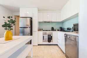 A modern kitchen with white cabinetry, stainless steel appliances, and a yellow vase on the counter.