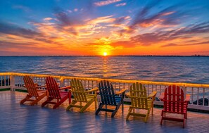 A sunset view from a deck with multiple Adirondack chairs.
