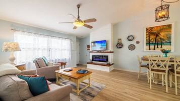 A living room with a sofa, coffee table, TV, and a dining area with chairs and a table.