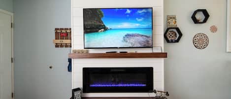 A living room with a flat-screen TV mounted above a fireplace, a mounted telephone, and decorative wall art.