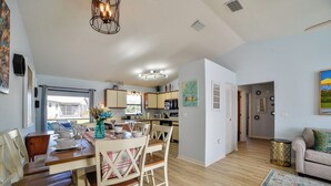 A spacious living area with a dining table, chairs, and a kitchen in the background.