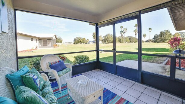 A sunlit room with a large glass door leading to a lawn, wicker furniture, and a ceiling fan.