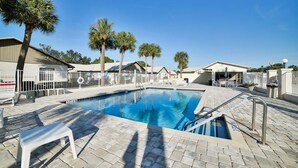A swimming pool with a tiled deck, surrounded by palm trees and a fence.
