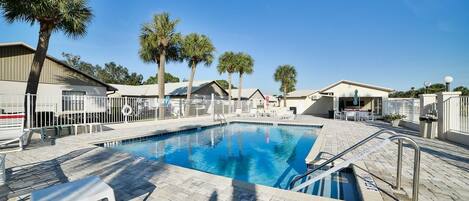 A swimming pool with a tiled deck, surrounded by palm trees and a fence.