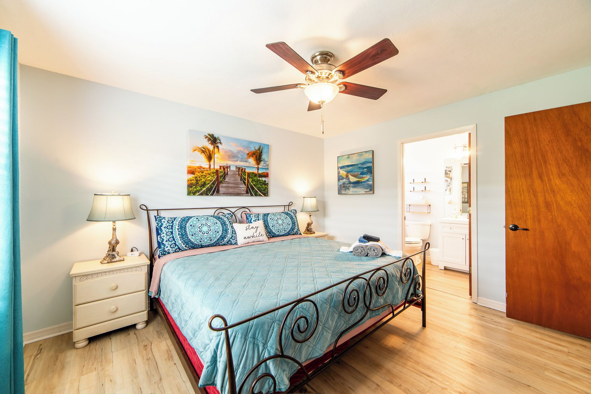 A bedroom with a bed, bedside tables, a ceiling fan, and artwork on the walls.
