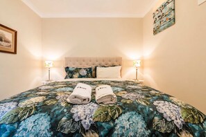A hotel room with a bed, two bedside lamps, a floral bedspread, and a framed picture on the wall. - Starlight Suite | Tekapo 1BR + Lake Walk (Lake Tekapo)