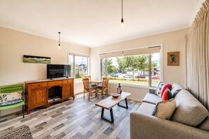 A modern living room with a television, wooden furniture, and large windows offering a view of the street. - Starlight Suite | Tekapo 1BR + Lake Walk (Lake Tekapo)