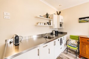 A modern kitchen with a stainless steel countertop, white cabinetry, and a small seating area with a green chair. - Starlight Suite | Tekapo 1BR + Lake Walk (Lake Tekapo)