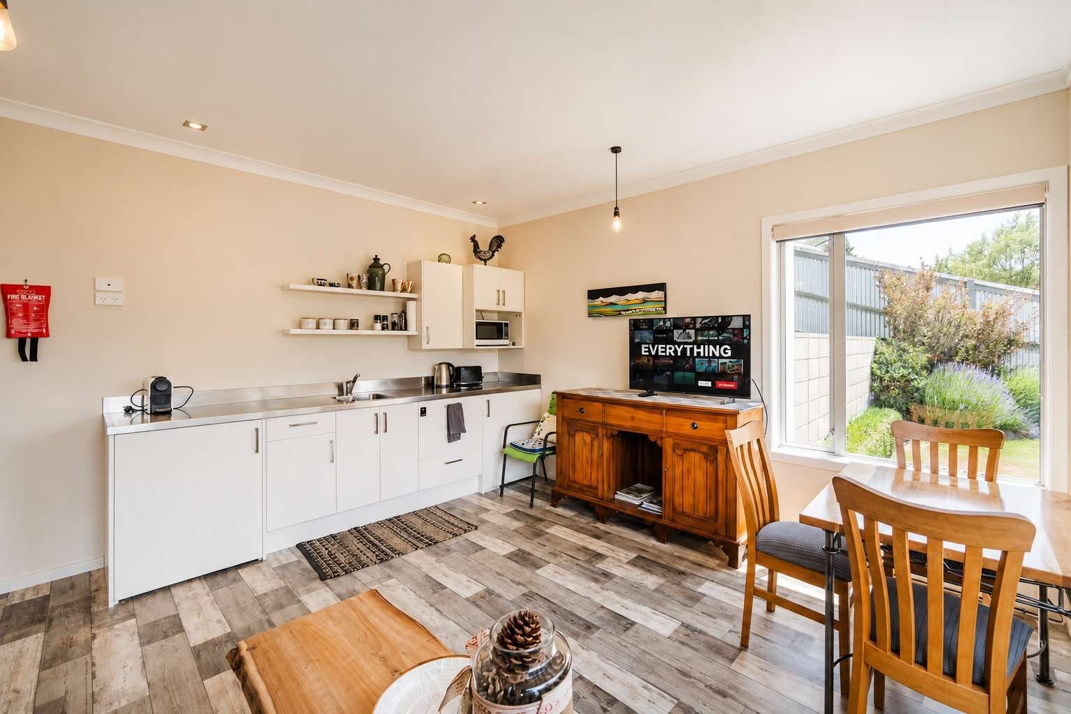 Une cuisine moderne avec des meubles blancs, une table à manger en bois avec des chaises, un téléviseur et un extincteur fixé au mur.