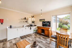 Une cuisine moderne avec des meubles blancs, une table à manger en bois avec des chaises, un téléviseur et un extincteur fixé au mur.