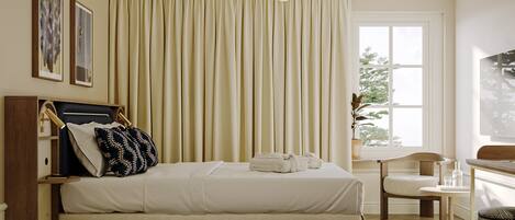 A bedroom with a bed, a chair, a desk, a window, and curtains.