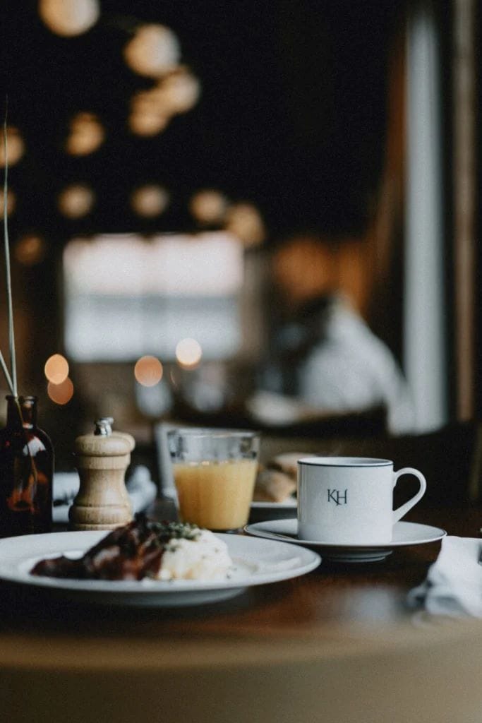 A table with a white mug, a glass of orange juice, and a plate with food.