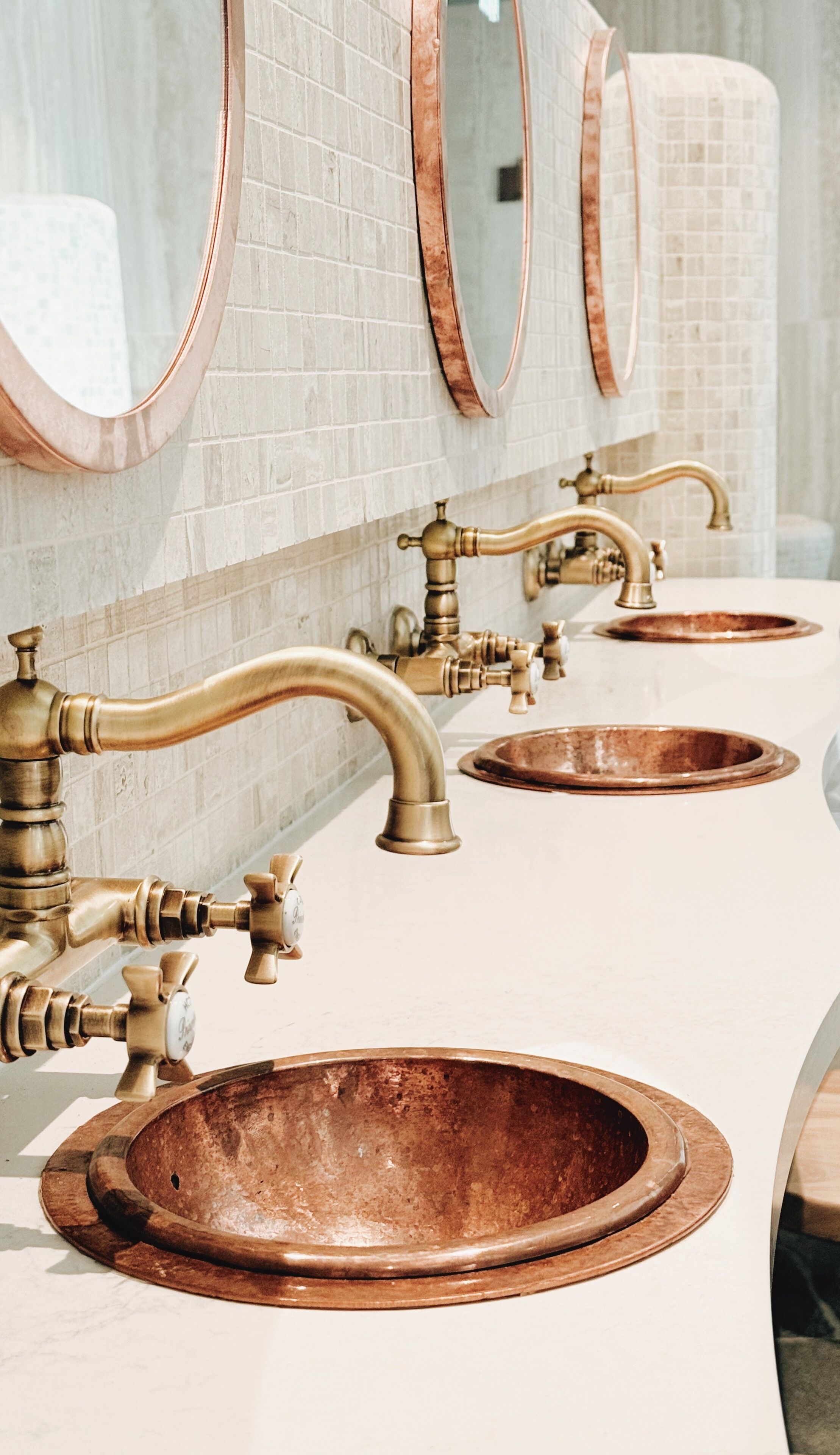 A bathroom with three sinks, each with a copper basin and a brass faucet.