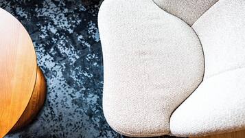 A close-up of a beige upholstered armchair with a textured fabric, positioned next to a round wooden table on a patterned rug.