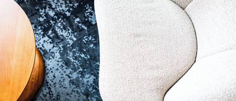 Primer plano de un sillón tapizado en beige con tela texturizada, ubicado junto a una mesa redonda de madera sobre una alfombra estampada.