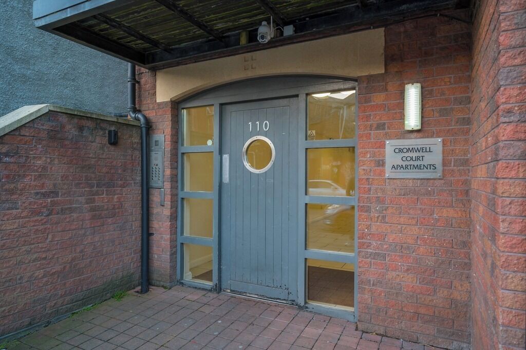 L’entrée d’un immeuble, avec une porte grise portant le numéro « 110 » et une enseigne indiquant « RÉSIDENCES CROMWELL COURT ».