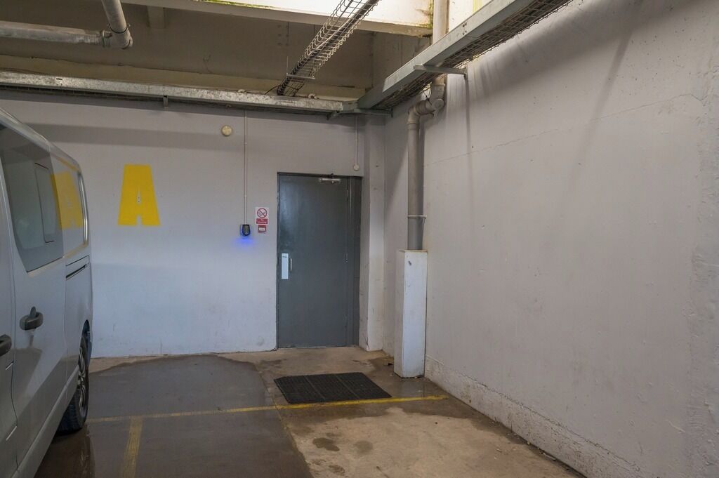 Un parcheggio con un muro bianco, una porta con il segnale rosso 'divieto di accesso' e un 'A' giallo segnalato.