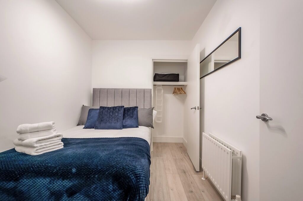 A small, modern bedroom with a bed, a bedside table, a wardrobe, and a mirror.