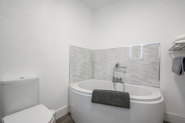 Un baño moderno con un inodoro blanco, una bañera independiente y un perchero con toallas.