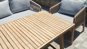 Una terraza con un muro de piedra, una mesa de madera y dos sillas con cojines.