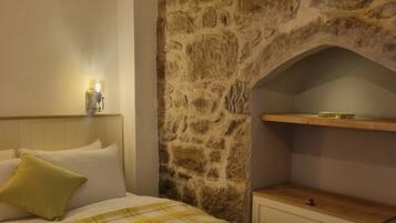 Ein Schlafzimmer mit Steinwand, einem Bett mit gelb-weißer Schachbrettdecke, einem Nachttisch und einer Wandleuchte.