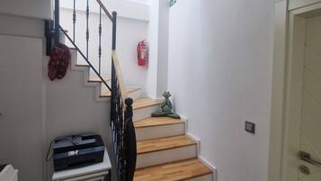 A staircase with wooden steps and a black railing, leading to a landing with a fire extinguisher and a framed picture on the wall.