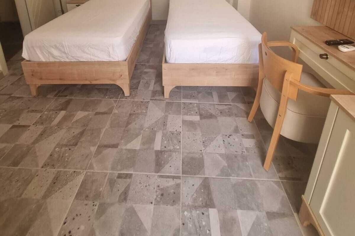 Habitación de hotel con dos camas de madera, un escritorio con silla, aire acondicionado y una lámpara.