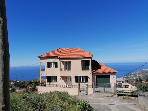 Um edifício de dois andares com telhado de telhas vermelhas, garagem e vista para o mar.