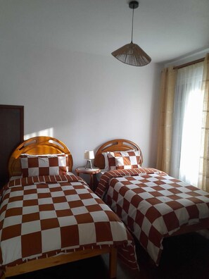 Quarto com duas camas, cada uma com colcha xadrez, mesa de cabeceira com abajur e luminária pendente.