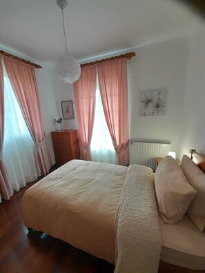 Quarto com cama, cortinas, radiador, cômoda e relógio de parede.