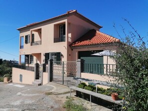 Uma casa de dois andares com telhado de telhas vermelhas, portão e um pequeno jardim.