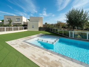 Une piscine dotée d’une terrasse en bois, entourée d’une clôture blanche et d’une pelouse.
