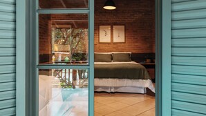 A bedroom with a brick wall, a bed with a green bedspread, two framed botanical prints, and a hanging light fixture. - Quinta de Brumado (Óleo)