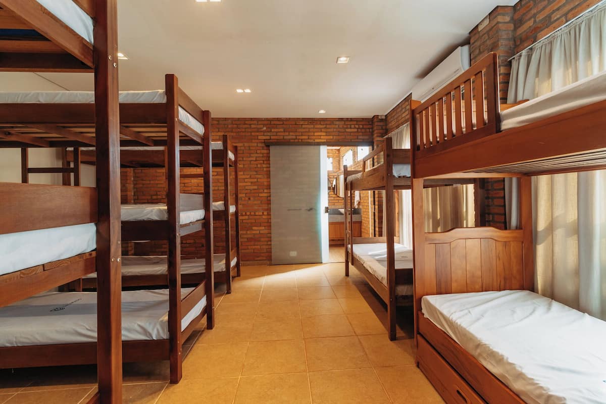 Habitación de albergue con literas, pared de ladrillo y suelo de baldosas.