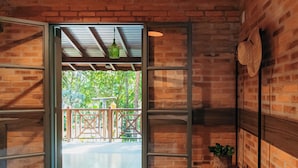 A bedroom with a bed, a wooden bench, wicker baskets, and a view of greenery outside. - Quinta de Brumado (Óleo)