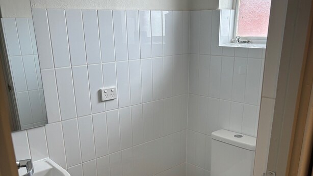 Ein Badezimmer mit weißen Fliesen, einem Waschbecken und einer Toilette.