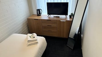 Et hotelværelse med en seng, et træskrivebord med et fjernsyn, en elkedel og et spejl.
