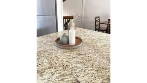 A kitchen counter with a granite surface, a stainless steel refrigerator, and a dining area with wooden chairs and a table.